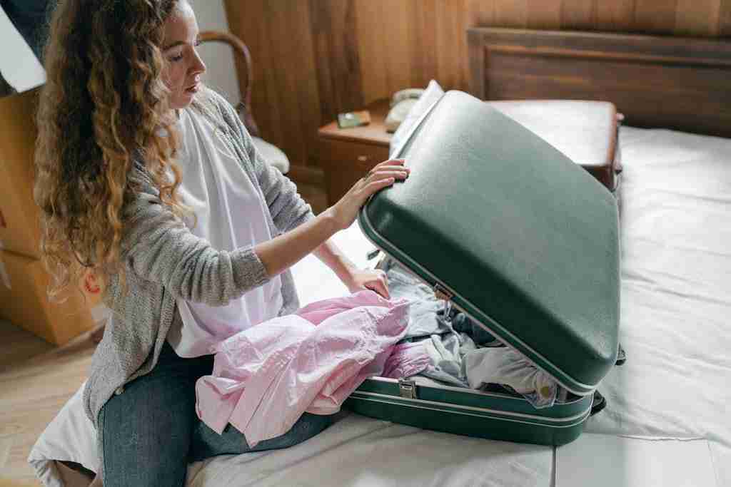 Focus woman packing suitcase on bed - try not to overpack when flying if you want to save on vacation expenses